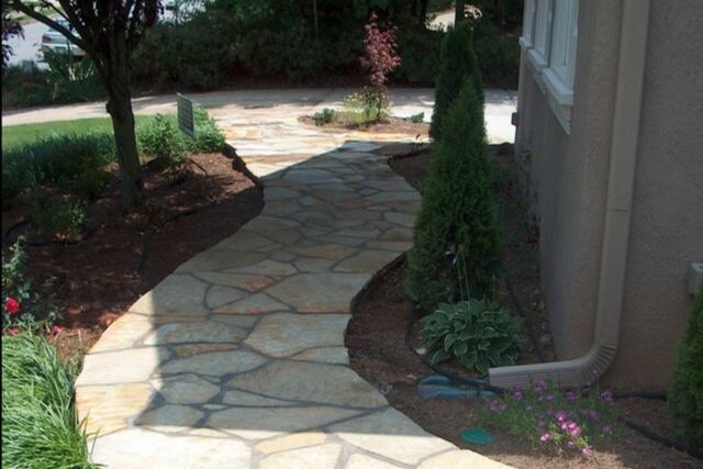 A curved flagstone walkway running alongside a house between planted garden beds